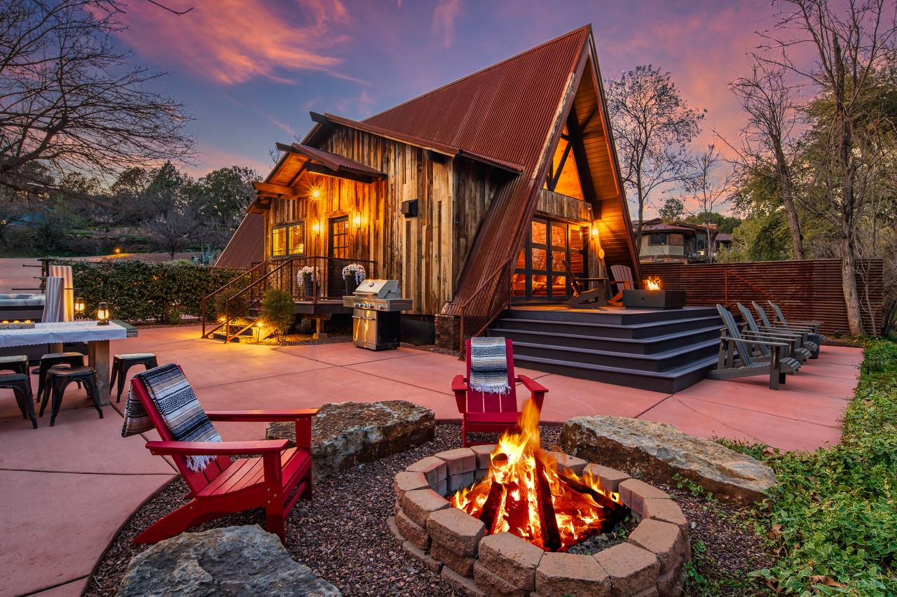 A-frame exterior at sunset with fire pit and red chairs